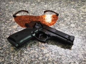 Photo of an airsoft gun and safety goggles orange in color, lying on the floor. Protection glasses are sitting behind the airsoft pistol in this picture.